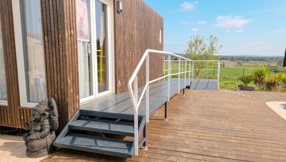 Rampe d'accès menant à une terrasse en bois près d'une construction moderne.